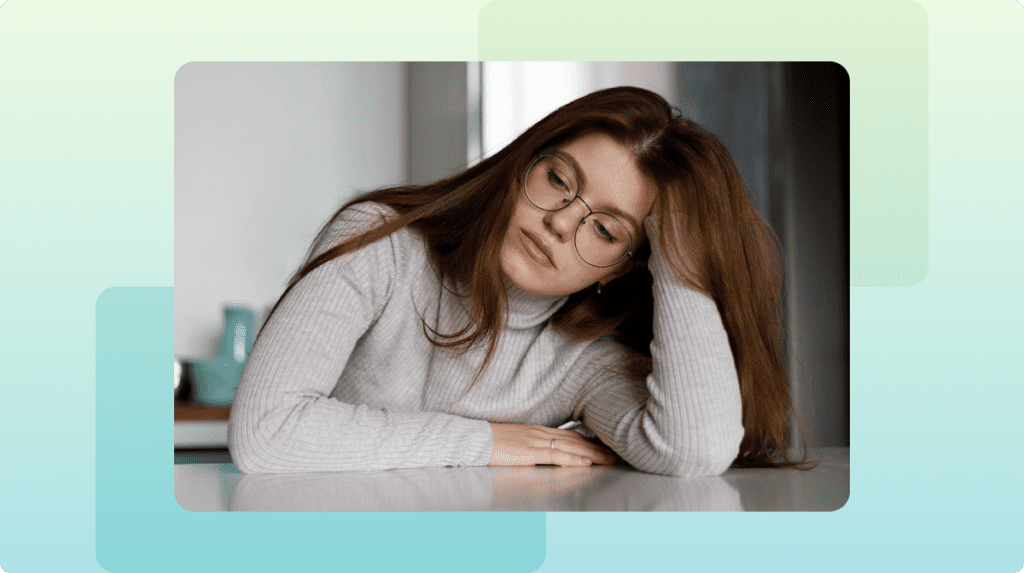 Person sitting at table with their head resting on their hand looking down.