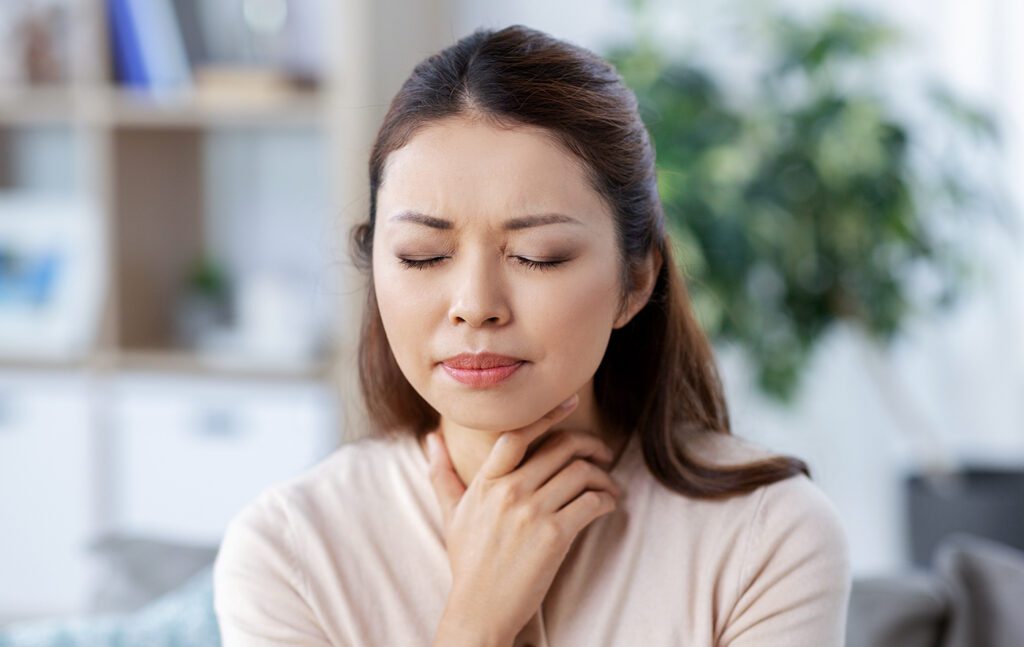 woman clutching her throat with her eyes closed appearing to be in distress