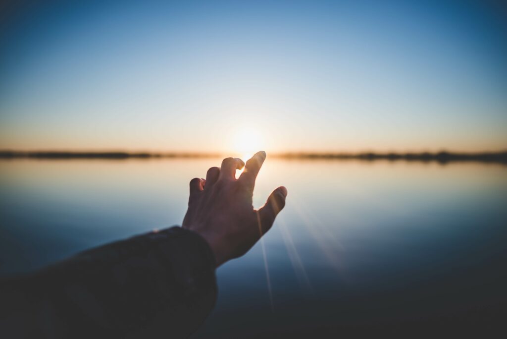 Hand reaching towards a sunrise